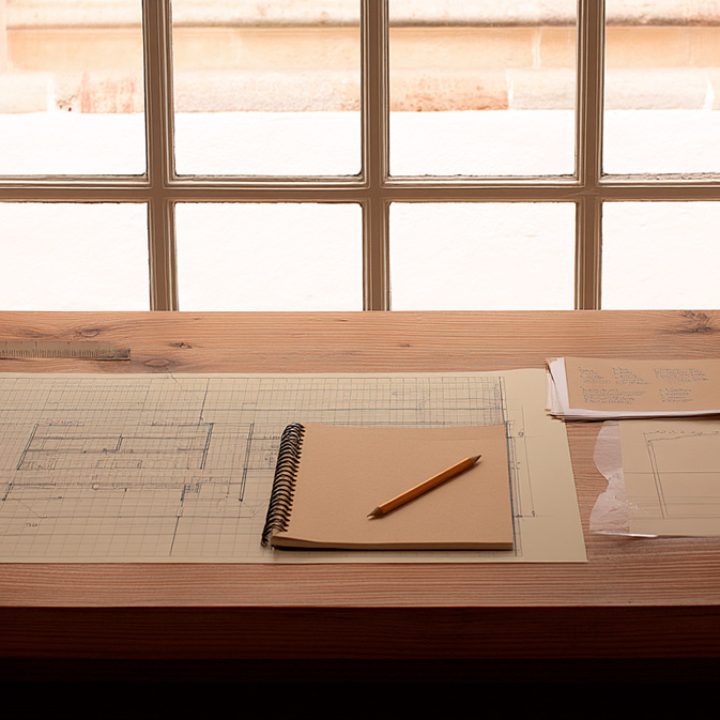 Mesa de trabajo con planos arquitectónicos, cuaderno y luz natural